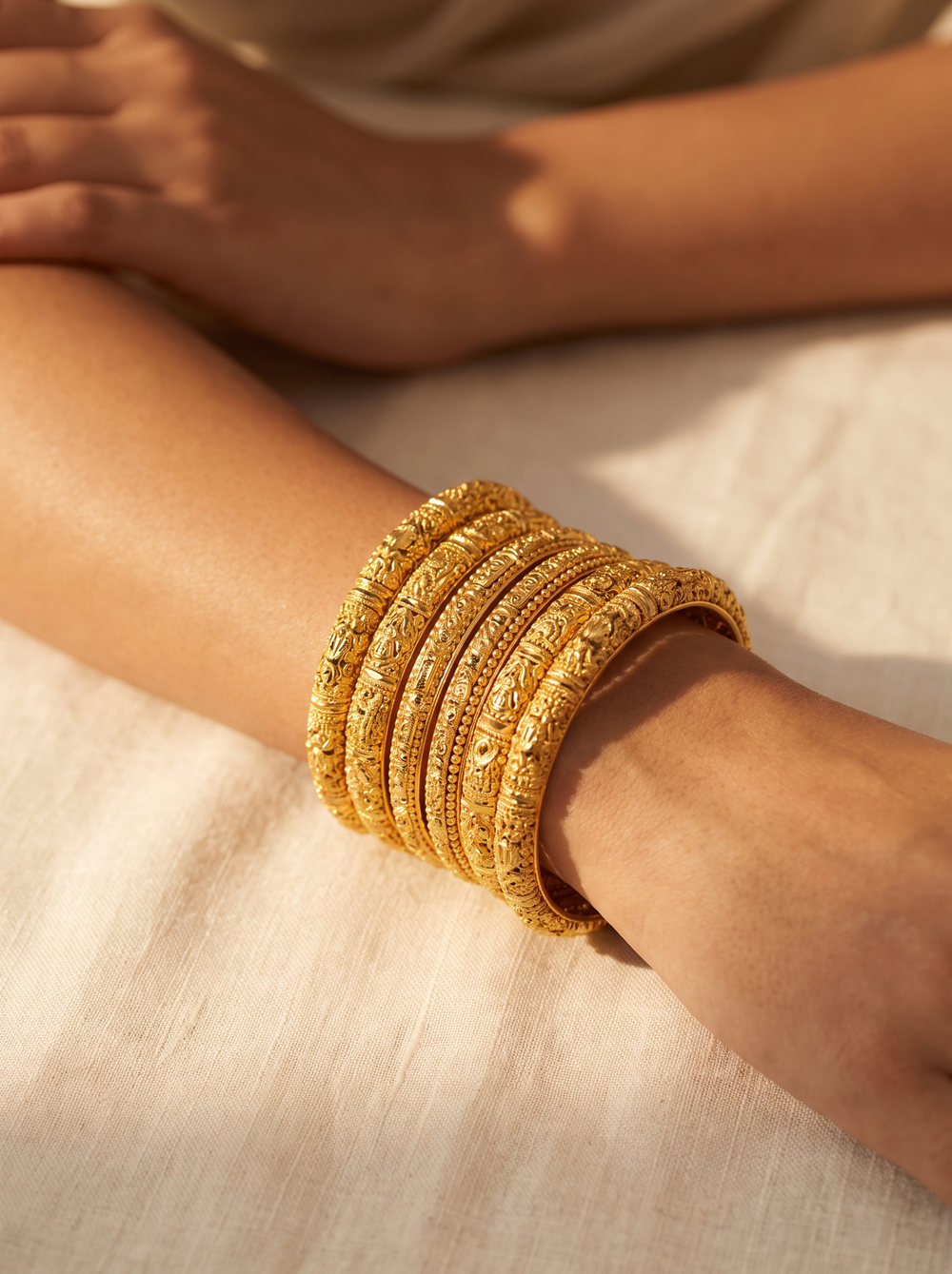 A woman's wrist stacked with patterned 22 carat gold bangles