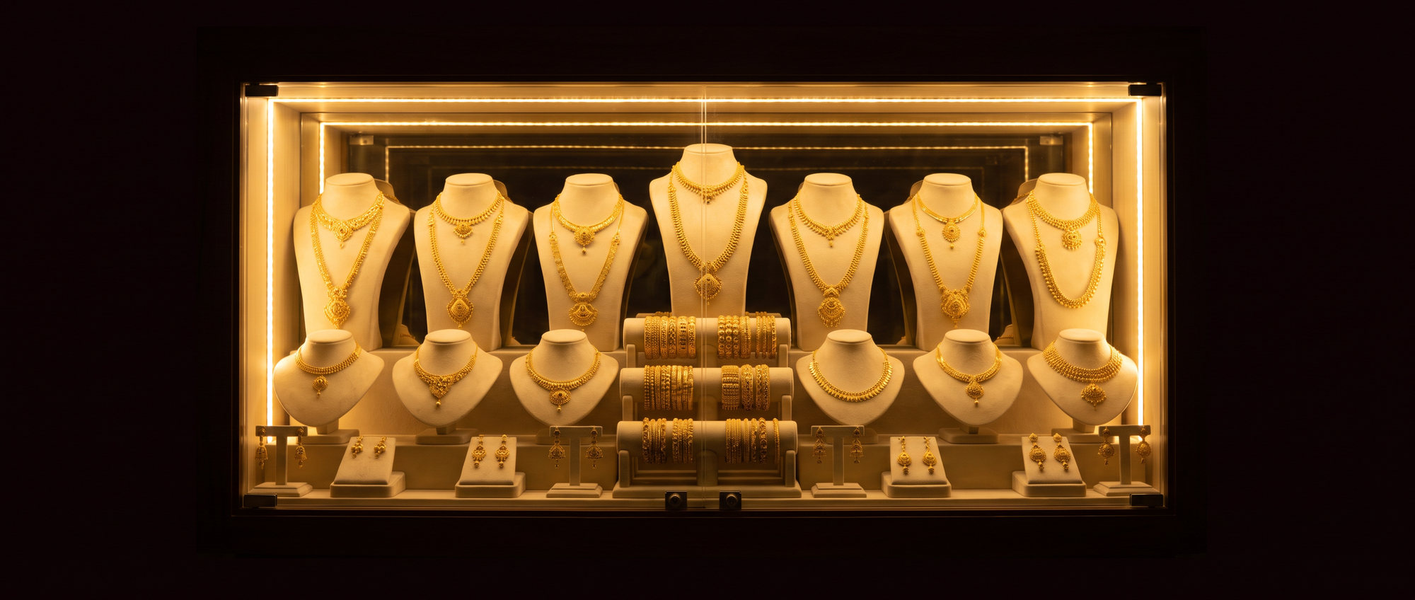 A lit display case of 22 carat gold on cream suede busts, the only bright thing in a dark room