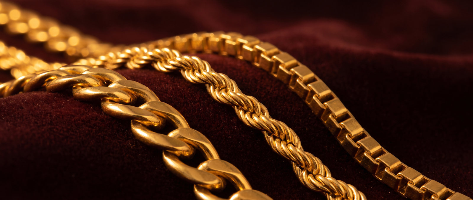 Three heavy gold chains of different links laid across maroon velvet