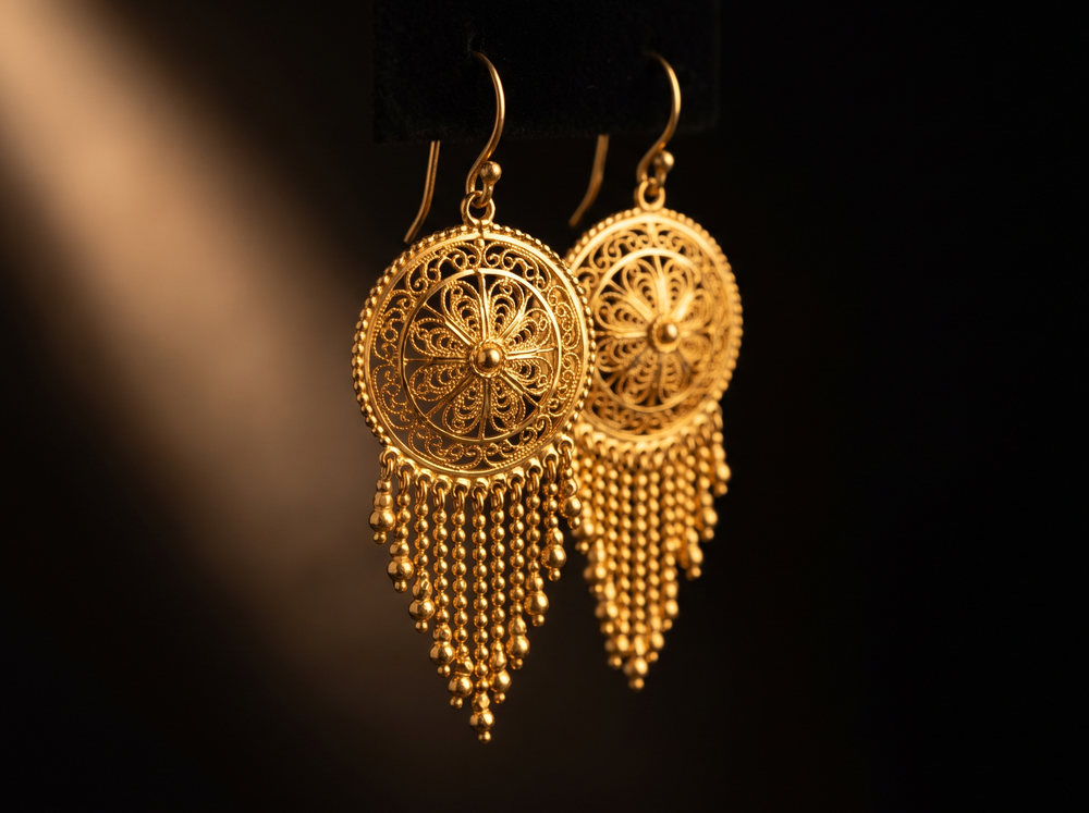 A pair of filigree gold drop earrings with beaded fringes on black