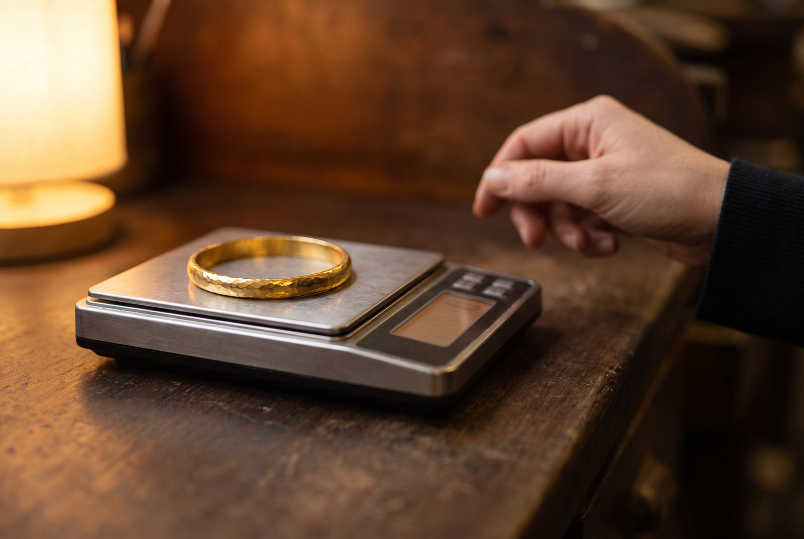 A heavy gold bangle resting on the steel pan of a jeweller's bench scale under a warm lamp