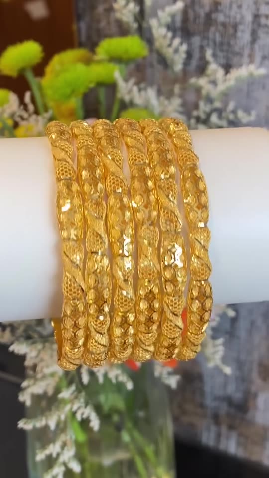 A stack of patterned 21 carat gold bangles on a white roll, turning under the shop lights