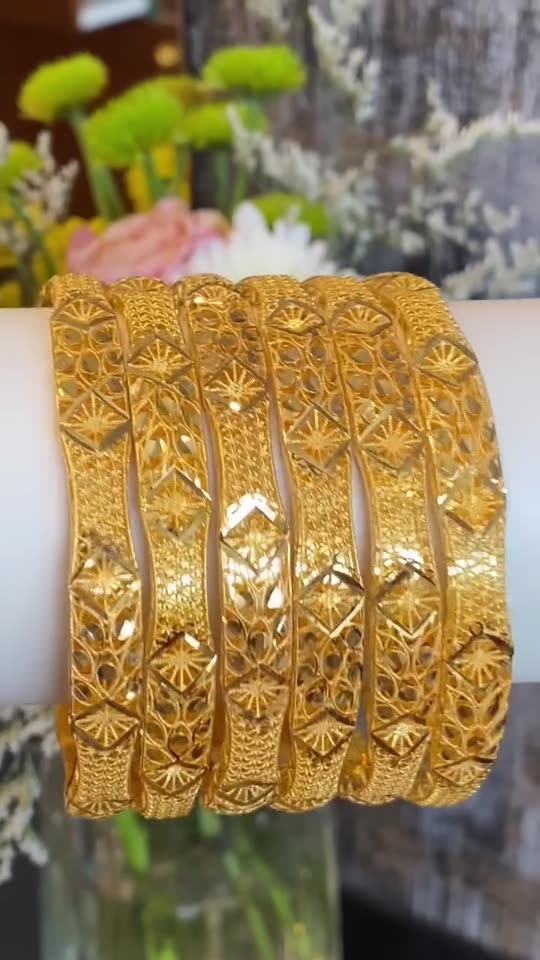 A stack of patterned 21 carat gold bangles on a white roll at Aroos Jewellers, turning under the shop lights