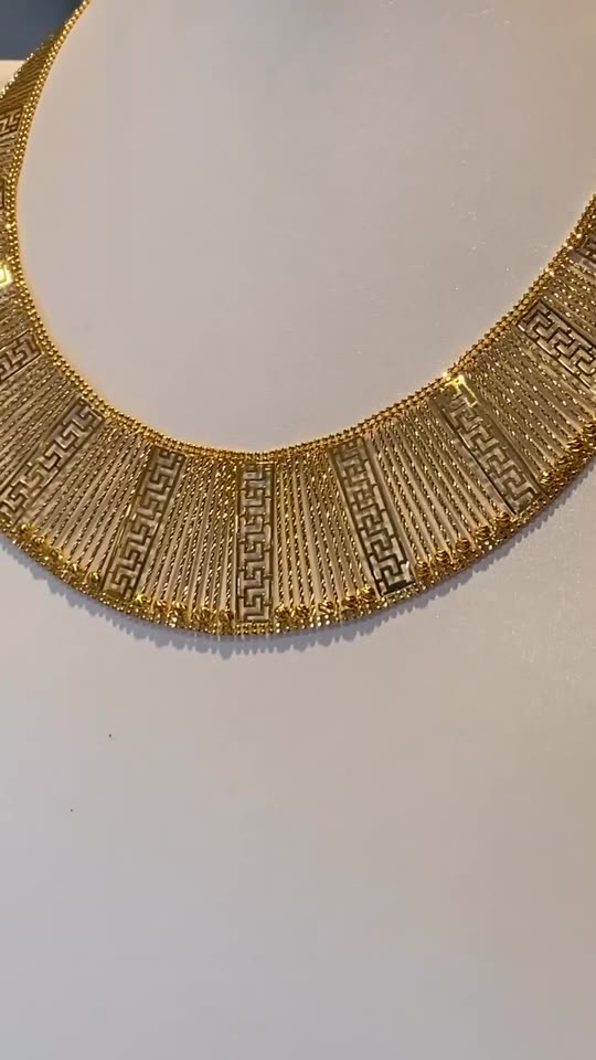 A wide 21 carat gold collar necklace on a white bust, the pattern catching the light