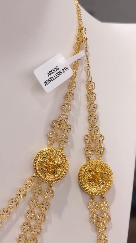 A 21 carat gold necklace with a fringed pendant and its matching earrings on a white bust