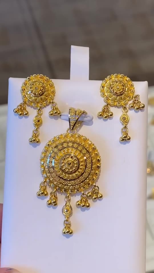 A large filigree 21 carat gold pendant and its matching earrings on a white stand