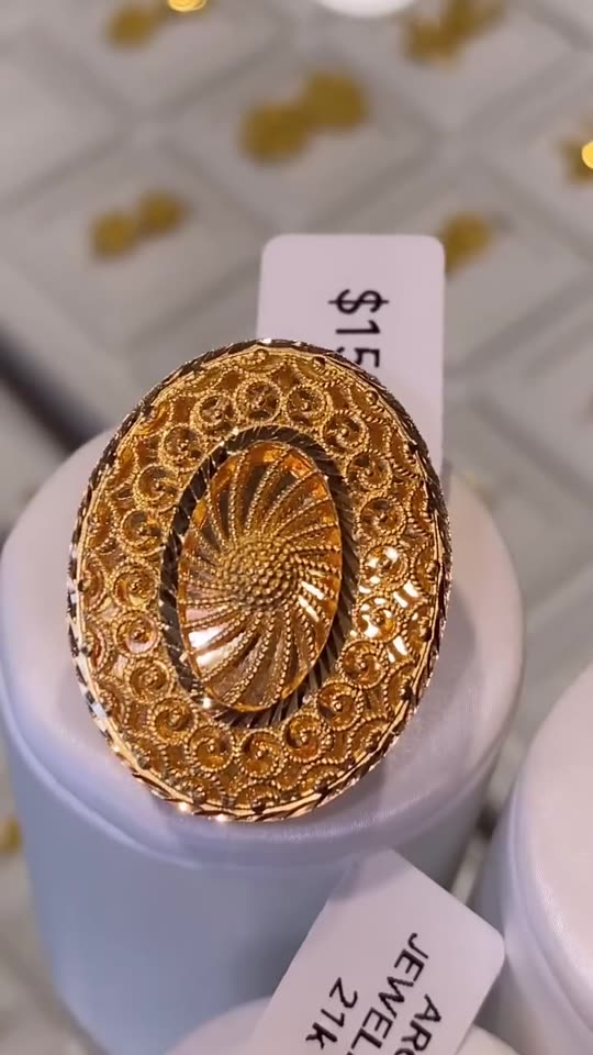 A 21 carat gold ring with an engraved marquise panel, close up on a white stand