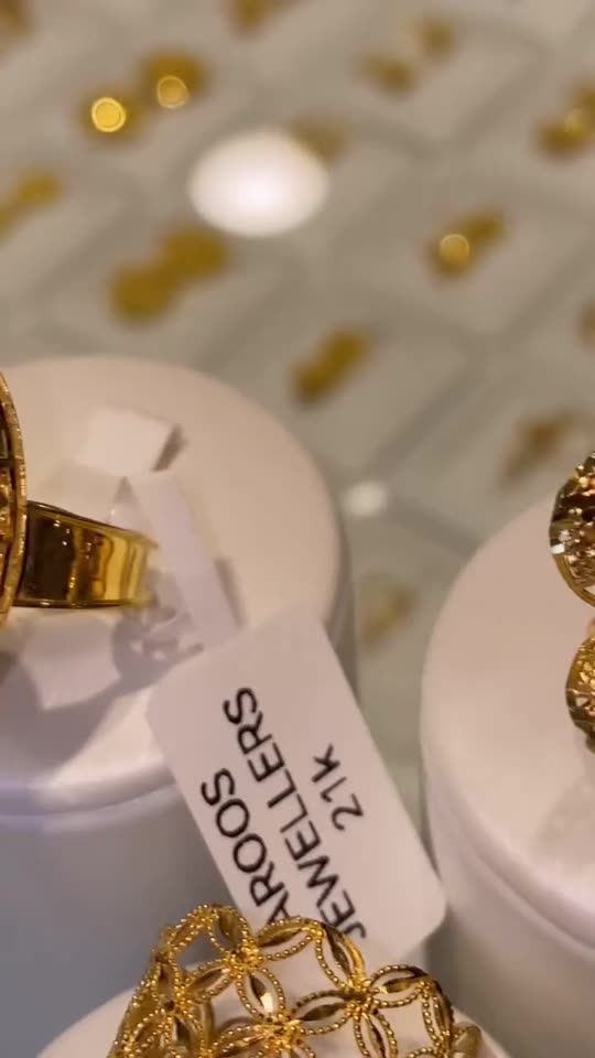 A marquise 21 carat gold ring with engraved panels on a white display stand