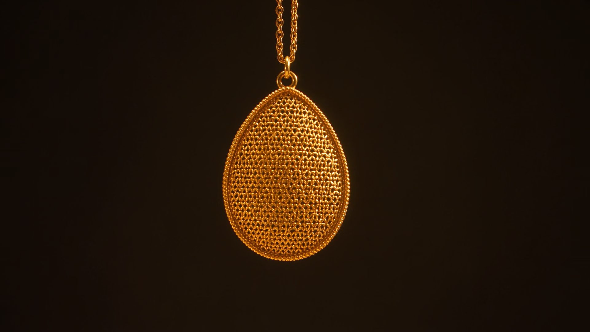 A pierced gold filigree pendant turning slowly under a bench lamp